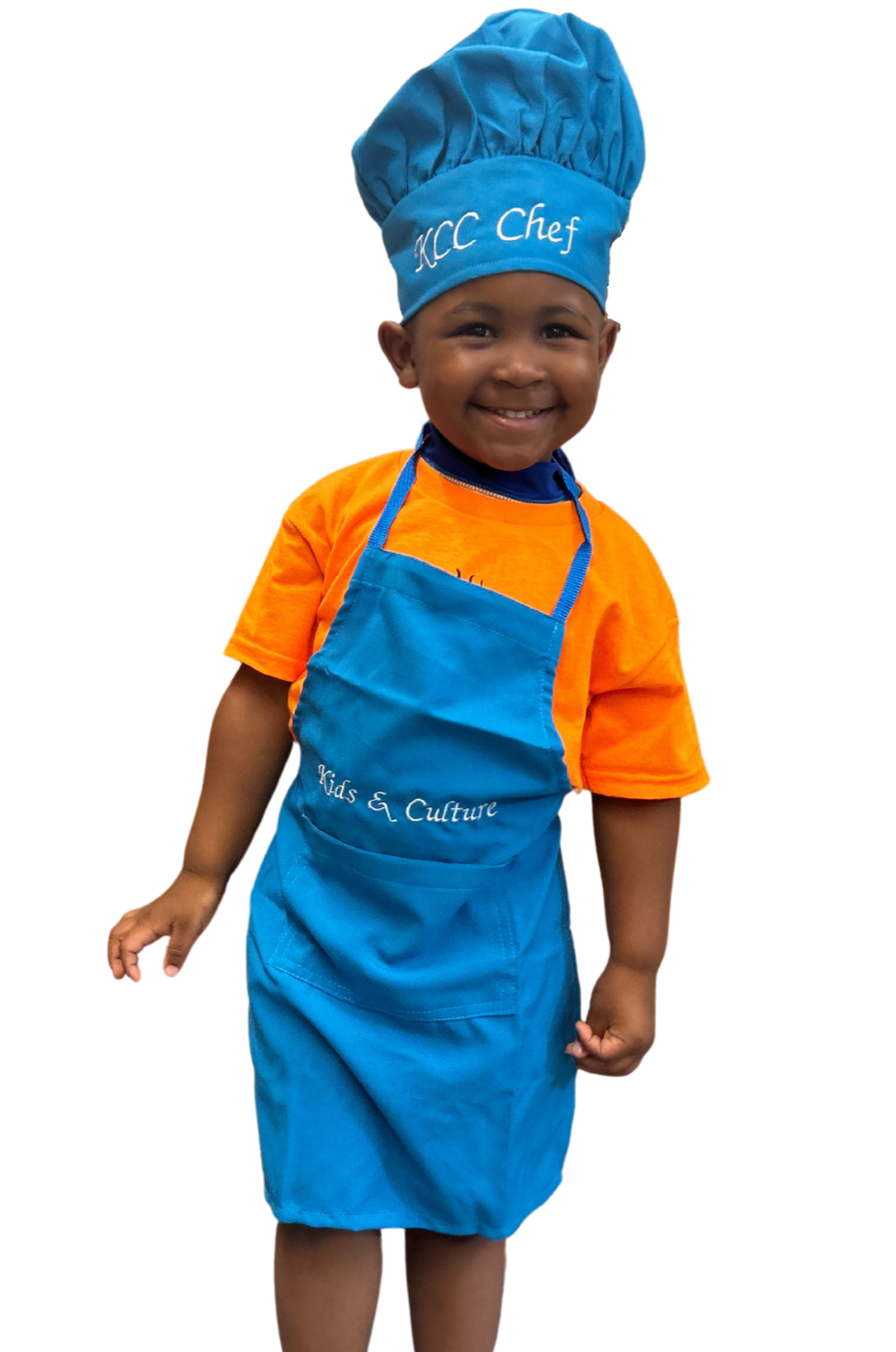 Child pictured wearing KCC arpon and hat set. Custom embroidered chef hat with the words “KCC Chef” on the hat and custom embroidered apron with the words “Kids & Culture” on the matching apron. The words are embroidered in white elegant font letters. The apron has a pocket on the front of the apron. Each hat is adjustable using velcro. The aprons and hats come in orange, red, turquoise, and hot pink